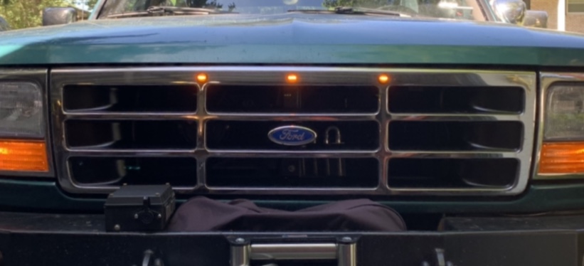 Front grille of a dark green Ford Bronco with chrome trim and amber marker lights.