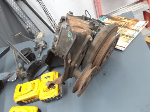 1994 Ford Bronco - A collection of vehicle parts, including a rusty transmission or transfer case with pulleys, two yellow DeWalt batteries, and other assorte…