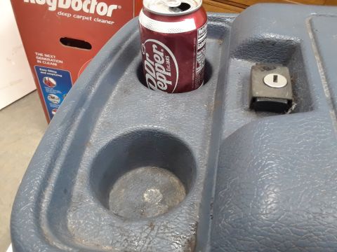 1994 Ford Bronco - A close-up view of a blue plastic center console with two cup holders. A can of Dr. Pepper is in one cup holder, and a small black latch is…