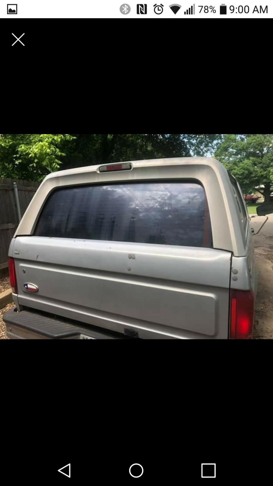 Rear view of a silver pickup truck with a white camper shell, Texas flag emblem on tailgate.