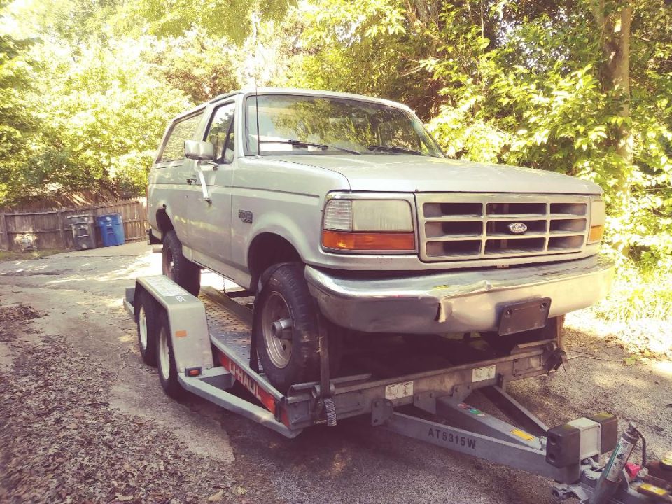 Silver 1990s Ford Bronco on a U-Haul trailer, front 3/4 view.