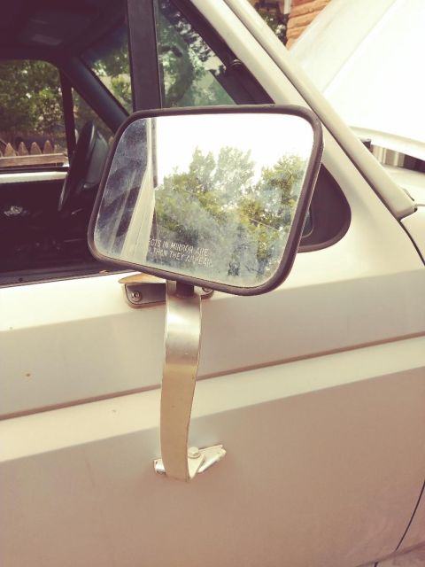 1996 Ford Bronco - Side mirror showing trees and the warning text 'Objects in mirror are closer than they appear'.