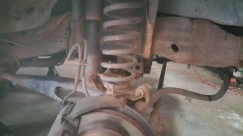 1996 Ford Bronco - Rusted rear suspension components of a vehicle, showing a coil spring and shock absorber.