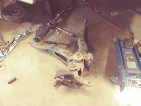 1996 Ford Bronco - Various vehicle suspension parts are laid out on the floor next to tools and a hydraulic jack.