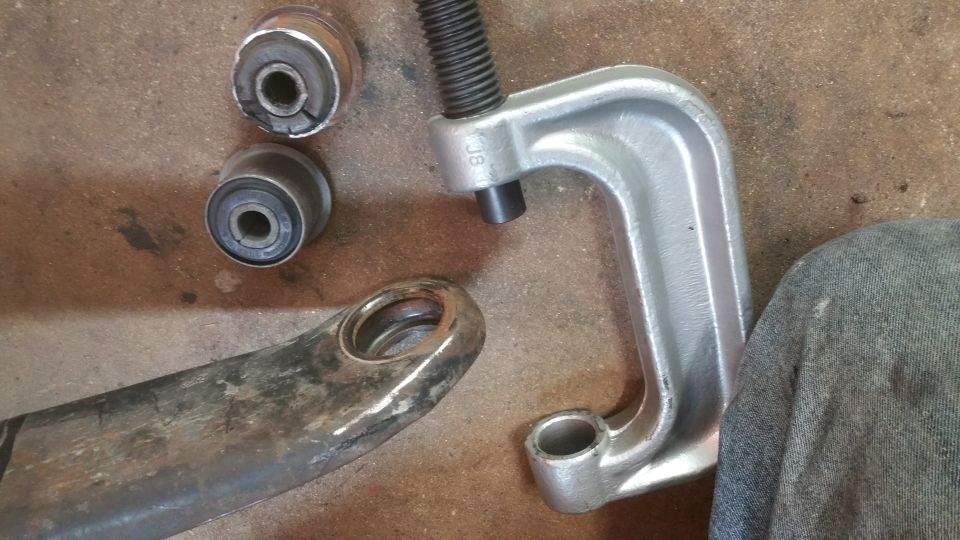 Ball joint separator tool and old suspension bushings next to a control arm