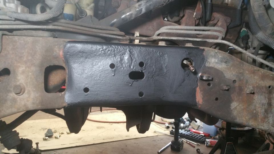 Close-up of a vehicle's frame section, partially painted black, with rust on other parts