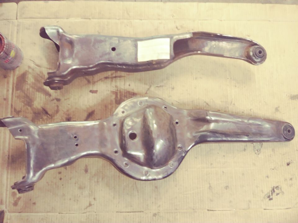 Two metal suspension components, one with a differential housing, laid out on a cardboard surface