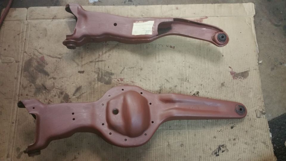 two reddish-brown painted suspension parts, one looks like a front control arm, the other a rear axle housing, laid out on cardboard