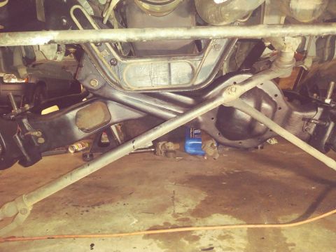 1996 Ford Bronco - Close-up of a vehicle's front suspension components and differential, with a blue fluid bottle visible on the garage floor.