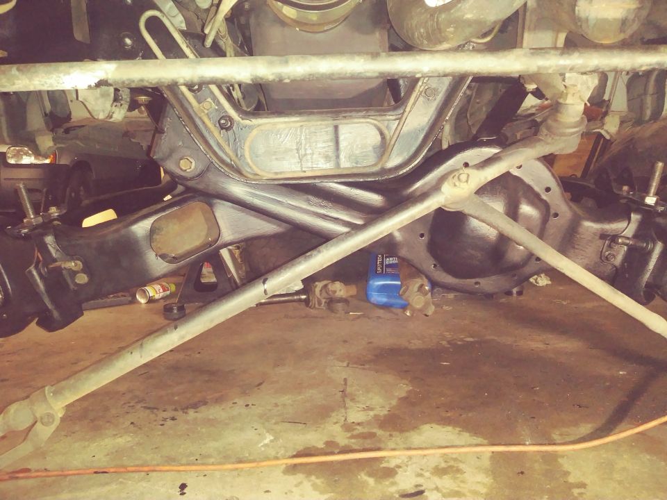 Underside view of a vehicle's front suspension and differential assembly, with a blue bottle of fluid on the floor