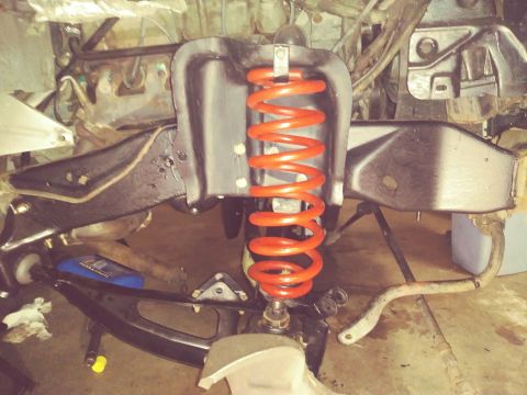 1996 Ford Bronco - Close-up view of a vehicle's front suspension system, a prominent orange coil spring and various metal components.
