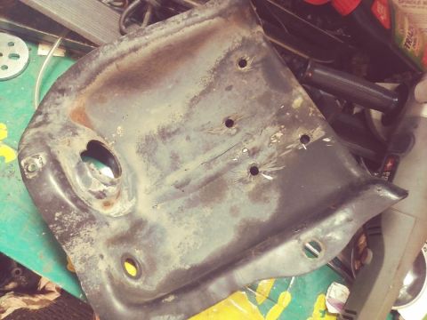 1996 Ford Bronco - A rusty metal part, possibly from a vehicle's front suspension, with several drilled holes and mounting points visible.