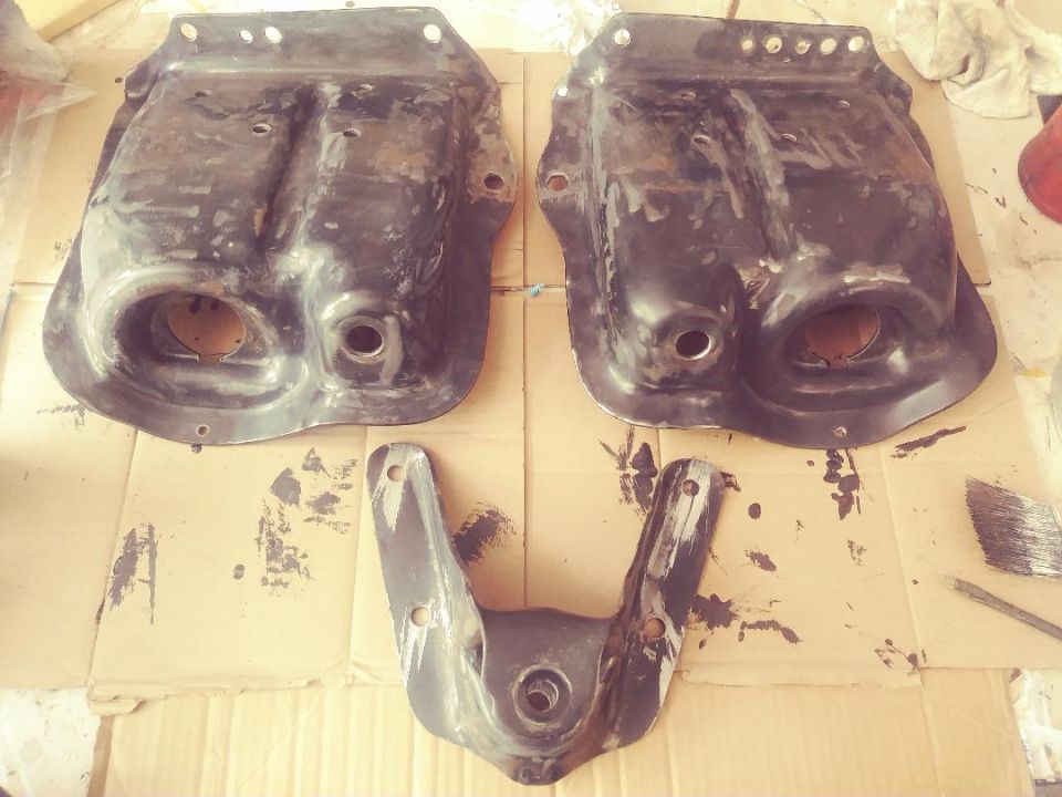 Two large, dark metal suspension components and one smaller, U-shaped bracket on a cardboard surface