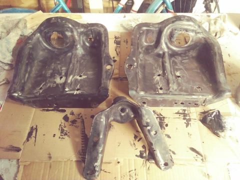1996 Ford Bronco - These metal parts, possibly from a vehicle's front suspension, are shown on a cardboard surface with some grease marks.