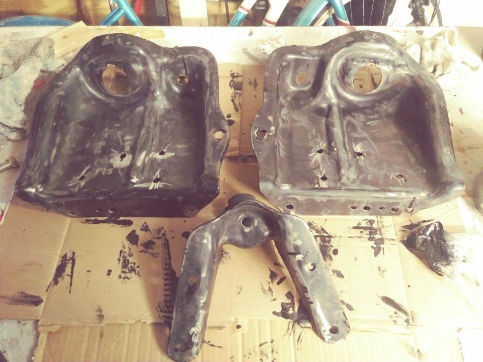Two large metal plates and a U-shaped bracket, likely suspension components, laid out on cardboard