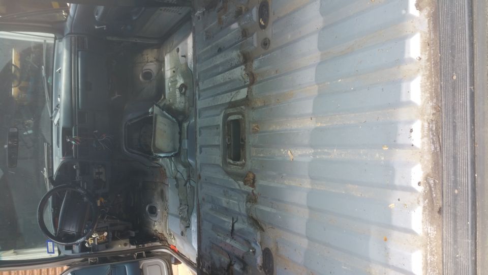 Vehicle interior with exposed metal panels, dashboard, and steering wheel visible. The interior appears stripped and weathered