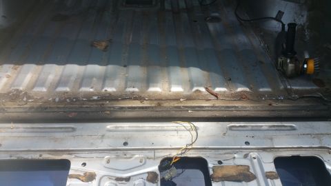 1996 Ford Bronco - The interior floor of a vehicle, showing some rust and a grinder tool.