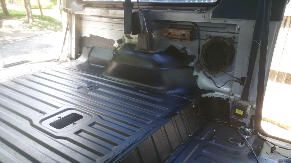Interior of a vehicle with bare metal floor and removed seats, showing speaker and seatbelt mechanism