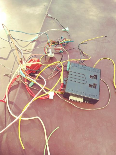 1996 Ford Bronco - A jumbled mess of wires and a black control module for a car alarm system are laid out on a textured surface.