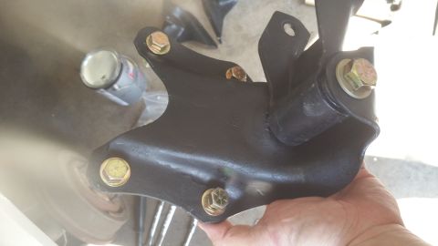 1996 Ford Bronco - A black metal suspension component with gold bolts is held by a hand, with a can in the background.