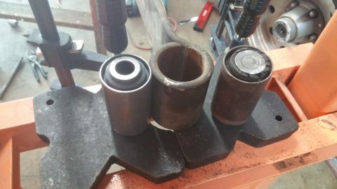 1996 Ford Bronco - Three suspension bushings and a metal sleeve are shown on a press, likely for removal or installation.