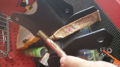 1996 Ford Bronco - Close-up of a tube of anti-seize lubricant and a bolt, with a vehicle part in the background.
