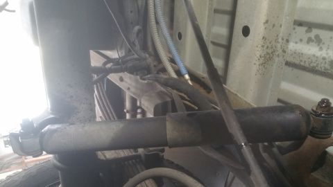 1996 Ford Bronco - Close-up view of the underside of a vehicle, focusing on the rear suspension system and associated plumbing and wiring.