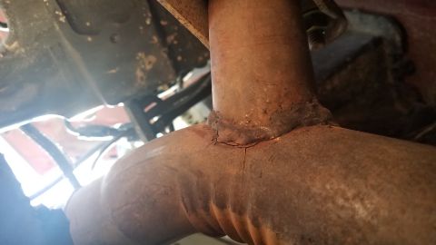 1985 Ford Bronco - Close-up view of a cracked weld on a rusty exhaust pipe.