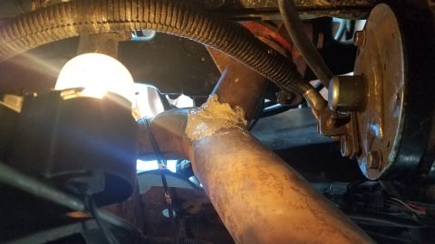 1985 Ford Bronco - Exhaust pipe repair with sealant. Visible wiring and hose suggest undercarriage or engine bay.