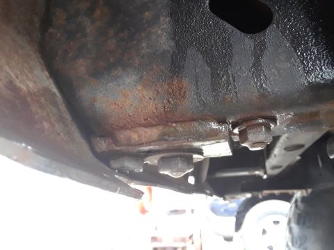 1985 Ford Bronco - Undercarriage view of a rusty vehicle frame, showing bolts and structural elements.