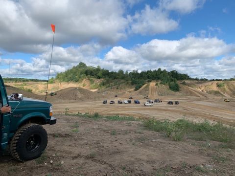 1996 Ford Bronco - Several off-road vehicles gather at a dirt park under a cloudy sky.