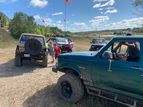 1996 Ford Bronco - A teal 1996 Ford Bronco is parked on a dirt road, with other vehicles and people around it on a sunny day.