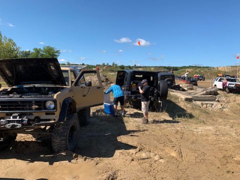 1996 Ford Bronco - People and multiple off-road vehicles are gathered on a dirt track under a clear blue sky.