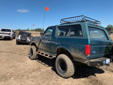 1996 Ford Bronco - A group of off-road vehicles, including a 1996 Ford Bronco, are seen on a dirt trail under a clear blue sky.