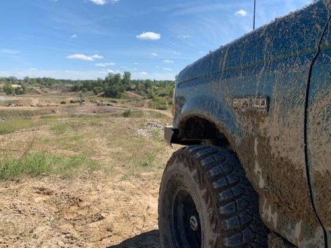 1996 Ford Bronco - A muddy 1996 Ford Bronco sits on an off-road course under a bright blue sky.