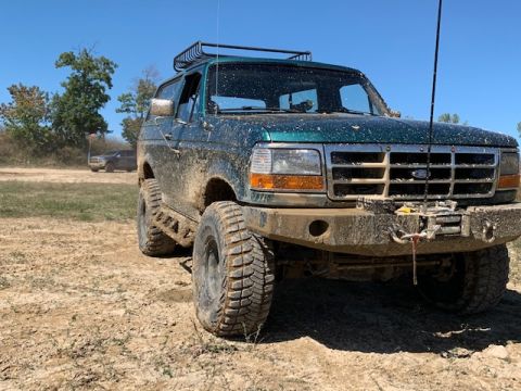 1996 Ford Bronco - This 1996 Ford Bronco, covered in mud, features off-road tires and a roof rack, suggesting it's ready for adventure.