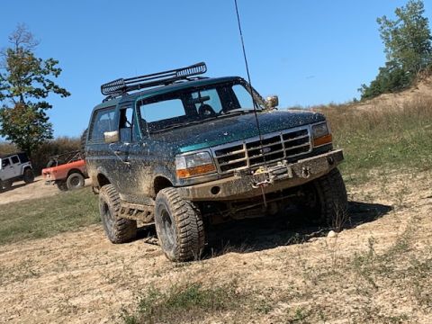 1996 Ford Bronco - A green Ford Bronco navigates a muddy off-road course with other vehicles in the background.