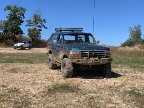 1996 Ford Bronco - This 1996 Ford Bronco is shown off-road, equipped with a roof rack and winch, under a clear blue sky.