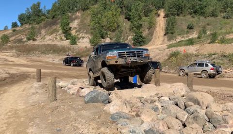 1996 Ford Bronco - A 1996 Ford Bronco tackles a challenging obstacle on an off-road trail, with other vehicles visible in the background.