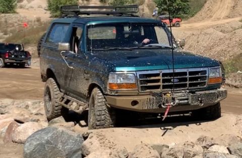 1996 Ford Bronco - A muddy 1996 Ford Bronco tackles an off-road course with other vehicles in the background.