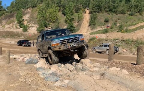 1996 Ford Bronco - A green Ford Bronco navigates a rocky obstacle course with other vehicles in the background.