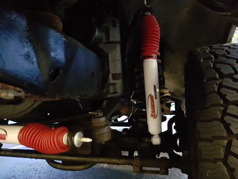 1978 Ford Bronco - A close-up, low-angle view of the undercarriage of a vehicle, showing two red and white Rancho RS5000 shock absorbers and a portion of a ti…