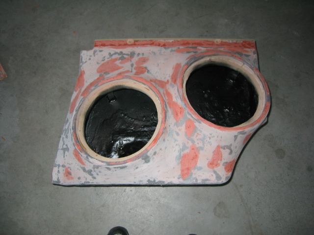 Raw fiberglass custom subwoofer box with two speaker cutouts in body filler on shop floor