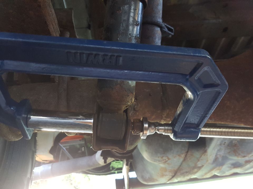 Blue Irwin C-clamp compressing a shock absorber bushing on the underside of a 1978 Ford Bronco.