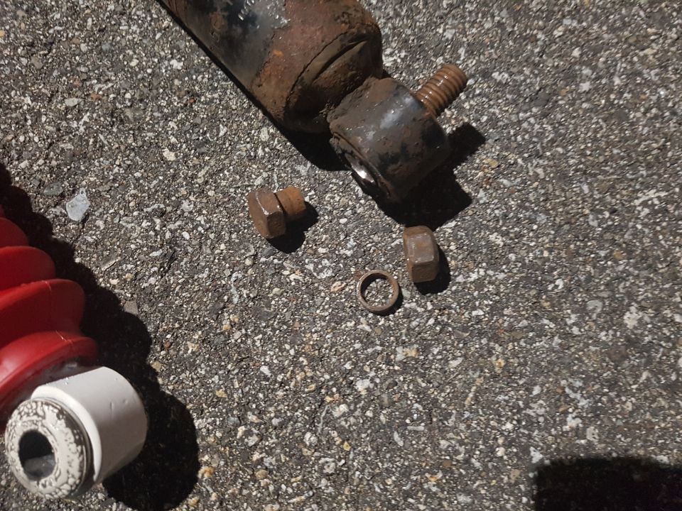 Rusty shock absorber parts and red bellows boot on a dark, textured surface.