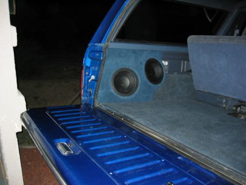 1989 Ford Bronco - Blue-carpeted subwoofer box holding two round speakers mounted in the rear cargo area of a blue vehicle, tailgate down.