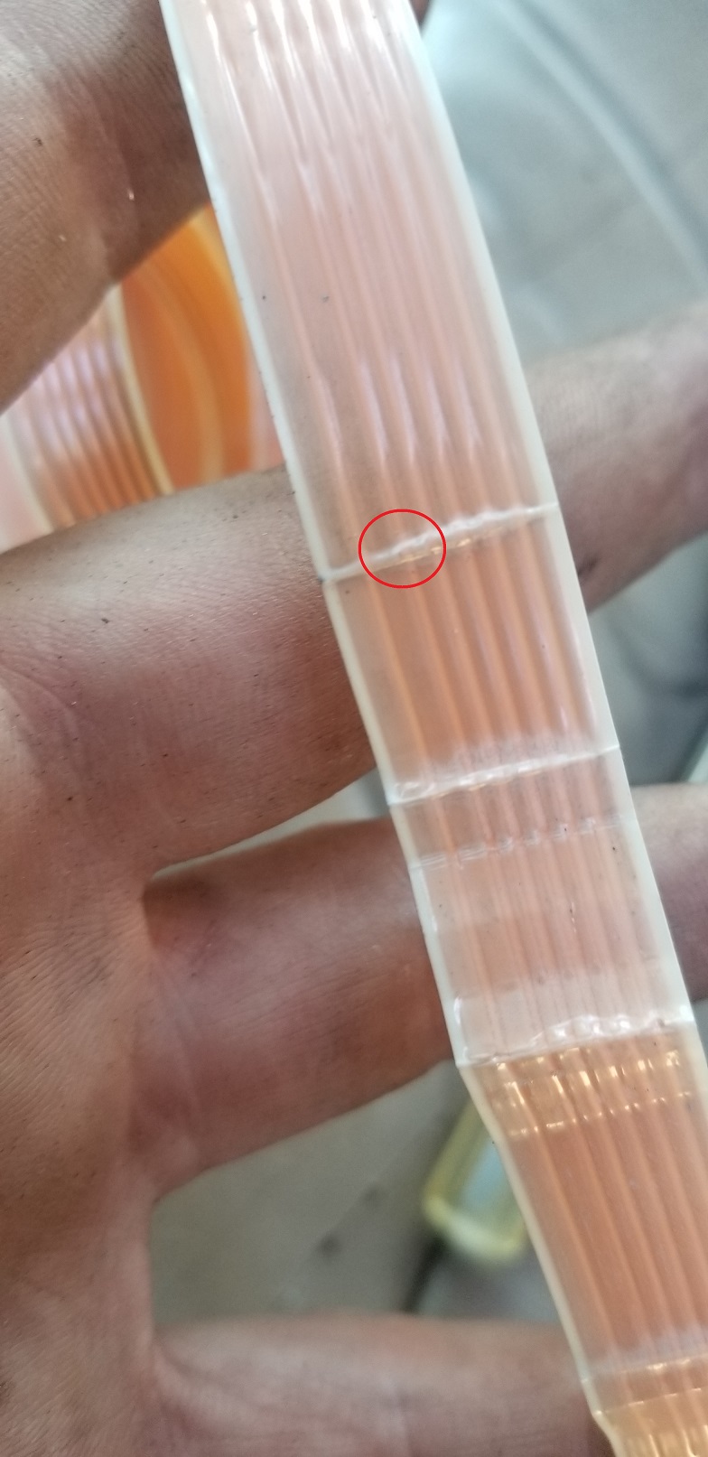 Close-up of a hand holding a clear tube with copper wires, showing a small break in the tube.