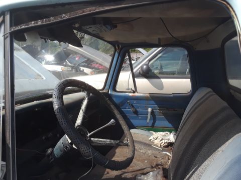 1994 Ford Bronco - Interior view of a vintage truck, showing a worn steering wheel, blue door panel, and striped seat. Other vehicles are visible through the…