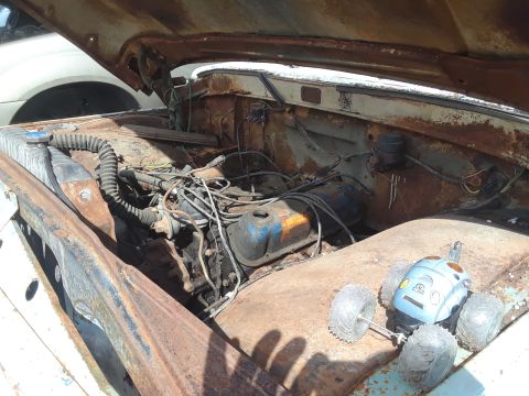 1994 Ford Bronco - The open hood of a heavily rusted classic pickup truck reveals a dirty engine bay with a small toy car resting on the fender. Visible parts…
