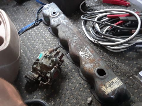 1994 Ford Bronco - A rusty valve cover and a carburetor sit on a patterned carpet next to a coiled set of jumper cables.